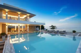 Sea Breeze Villa Pattaya modern exterior with large swimming pool and ocean view at dusk.