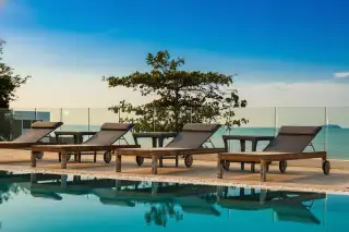 Sea Breeze Villa Pattaya poolside lounge chairs reflecting in the water against a vibrant sunset sky.