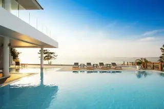 Sea Breeze Villa Pattaya large swimming pool overlooking the ocean with sun loungers and a modern building.