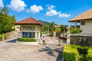 Hill View Villas sign with blue letters on a white wall, green leaf logo, and lush green bushes below.