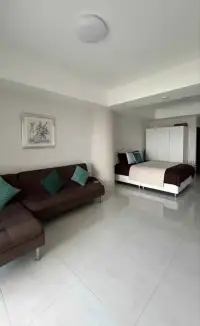 Studio Condo for Sale at Sky Beach open living area with sectional sofa and bed, glossy tile floor