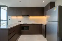 1 Bedroom Condo for Rent at Panora Estuaria U-shaped kitchen with dark wood cabinets, induction hob, built-in microwave and stainless steel fridge