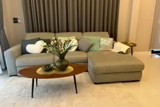 SP Village 1 living room with grey L-shaped sectional sofa, decorative cushions, and oval wooden coffee table