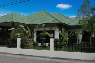 SP Village 4 single-story house exterior with green tiled roof, white fence, and tropical plants in Pattaya.