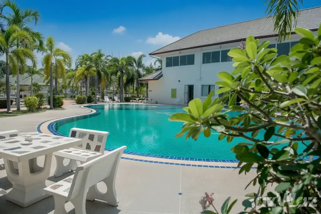 SP Village 5 large curved swimming pool with blue tiles, surrounded by palm trees and a white clubhouse.