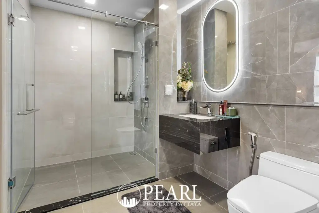 2 Bedroom Grand Executive Condo for Sale at Aquarous Jomtien Pattaya: Modern bathroom with glass shower, floating vanity, and illuminated mirror.