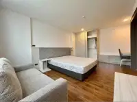 2 Bedroom Condo for Rent at Stasia Dormy Residence bedroom with gray tufted headboard, sofa, and hillside window view