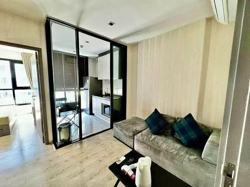 1 Bedroom Condo for Sale at The Base Central Pattaya living room with gray sofa and glass-partitioned kitchen