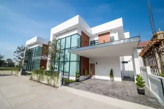 The Image shows a close-up of the modern white house exterior with large windows, wooden accents, and blue sky.