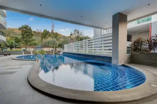 The Lofts Pratumnak covered swimming pool area with blue tiles, lush green hills, and distant buildings.