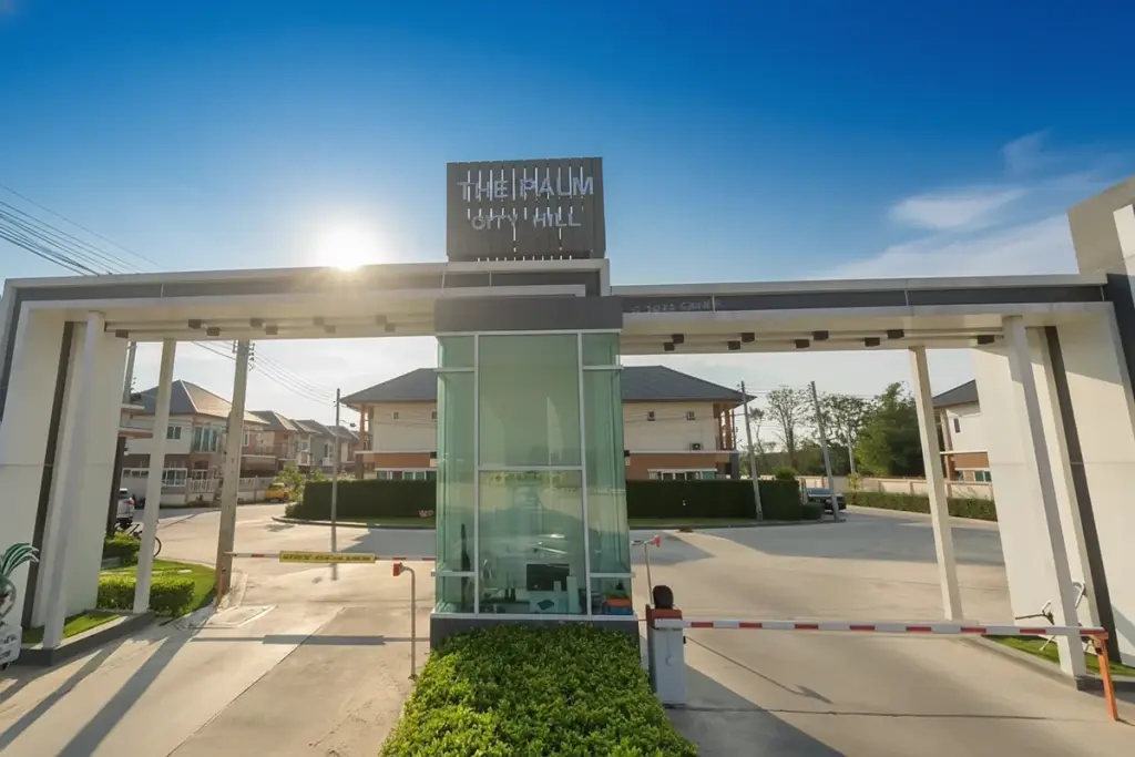 The Palm City Hill main entrance gate with a security booth and barrier, leading into a residential area with houses.