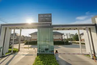 The Palm City Hill main entrance gate with a security booth and barrier, leading into a residential area with houses.