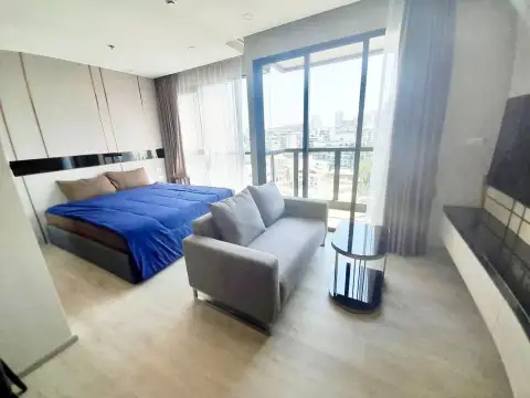 Studio Condo for Rent at The Panora Pattaya bedroom with blue bed, gray sofa and floor-to-ceiling city view window