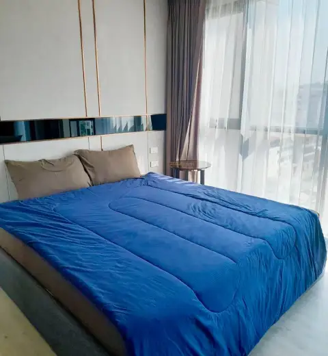 Studio Condo for Rent at The Panora Pattaya king bed with blue comforter beside sheer curtained window
