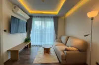 1 Bedroom Condo for Rent at The Peak Towers living room with beige sofa, TV, and city view through sheer curtains