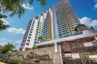 The Peak Towers high-rise condominium building with multiple balconies, surrounded by green trees, overlooking the ocean.
