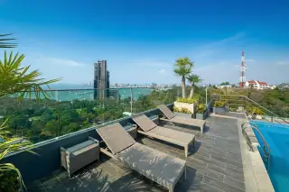 The Point Pratumnak rooftop terrace with sun loungers, palm trees, and a panoramic ocean and city view.