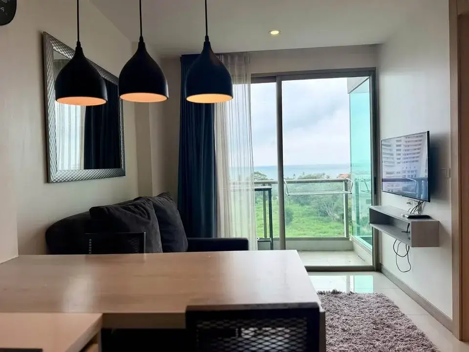 1 Bedroom Condo for Rent at The Riviera Jomtien living area with sofa, dining table and sea view balcony