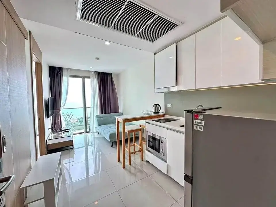 1 Bedroom Condo for Rent at The Riviera Jomtien open-plan kitchen with white cabinets and living area with sea-view balcony
