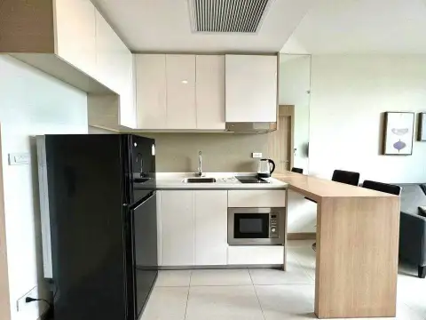 1 Bedroom Condo for Sale at The Riviera Jomtien white kitchen with black refrigerator and wooden breakfast bar