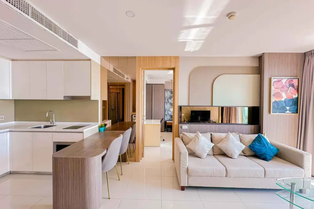 2 Bedroom Condo for Rent at The Riviera Jomtien open-plan kitchen with white cabinetry and living room with beige sofa