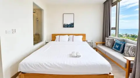 Studio Condo for Rent at The Riviera Jomtien bedroom with king bed, gray sofa and sea-view window