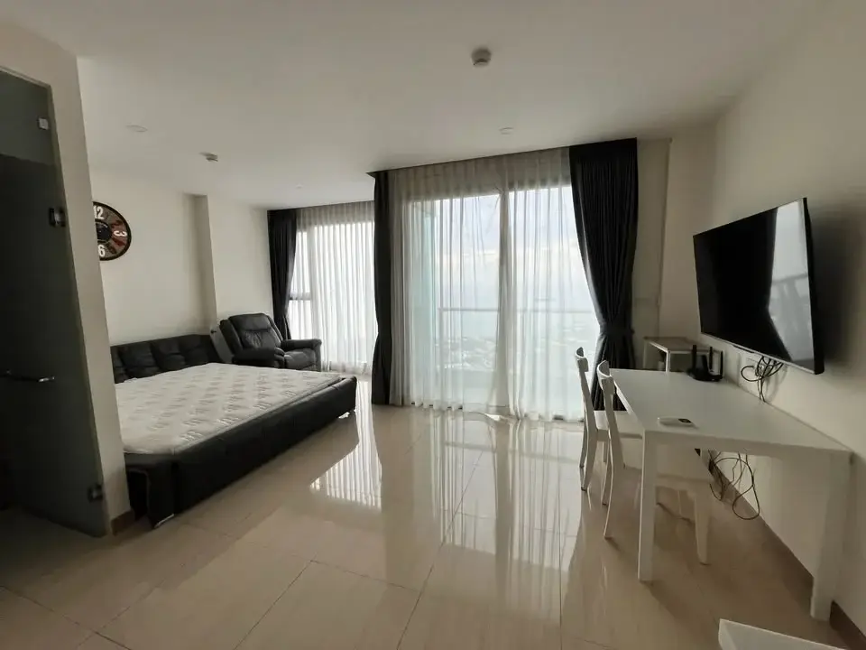 Studio Condo for Rent at The Riviera Jomtien bedroom with sofa, TV, and sea-view balcony window