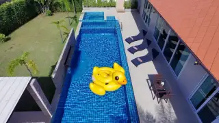 The Ville Jomtien long private swimming pool with outdoor dining area and house exterior at dusk.