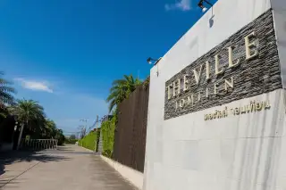 The Ville Jomtien main entrance gate with large stone sign under a clear blue sky.