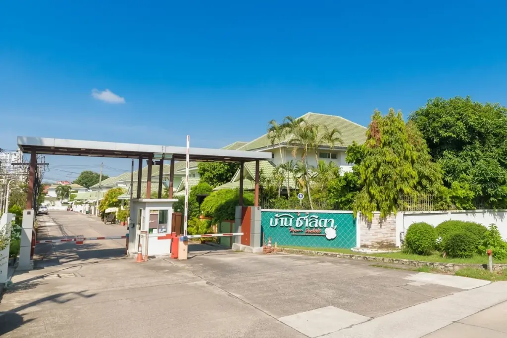 Baan Chalita 1 main entrance gate with security booth, barrier arms, and a green welcome sign with Thai script.