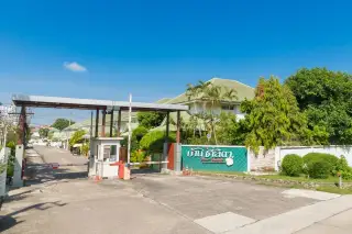 Baan Chalita 1 main entrance gate with security booth, barrier arms, and a green welcome sign with Thai script.