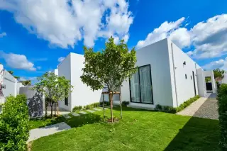 Serendipity Villas modern white house with green lawn, young trees, and gravel path under a blue sky.