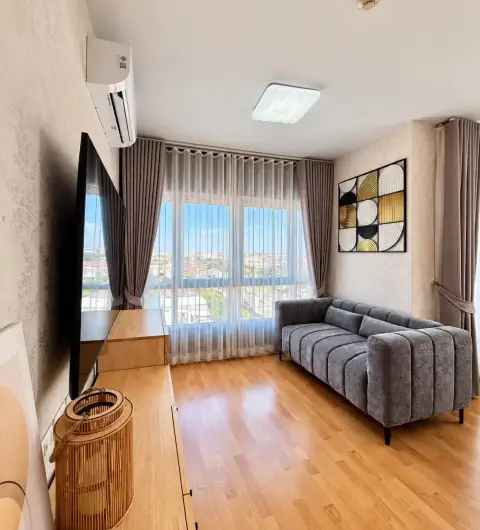 2 Bedroom Condo for Rent at Unicca living area with gray sofa, city view window, and wall art decor