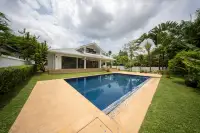 4 Bedroom House for Sale in Nong Prue, exterior view showing the pool, surrounding garden, and tropical trees.