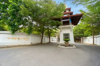 Nagawari Pattaya main entrance gate with white wall, gold lettering, traditional Thai-style security booth, and lush green trees.