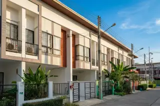 Patta Town modern townhouse exterior with gray, white, and red facade, black-framed windows, a dark metal gate, and a palm tree.