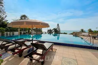 Baan Rimpha swimming pool area with blue and white striped umbrella, wooden sun loungers, and lush greenery.