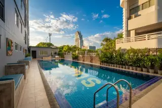 Trio Gems outdoor swimming pool with blue tiles, yellow 'GEMS' lettering, and surrounding buildings under a cloudy sky.