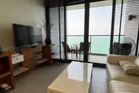 1 Bedroom Condo for Sale at Zire Wongamat living room with TV, sofa, and balcony with ocean view.