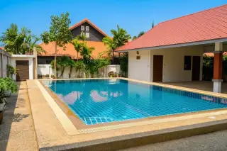 Baan Suan Neramit 2 outdoor seating area overlooking a blue swimming pool, surrounded by tropical plants and houses with orange tiled roofs.