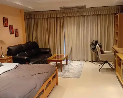 Studio Condo for Rent at View Talay 5D open-plan living area with bed, black leather sofa, and curtained window