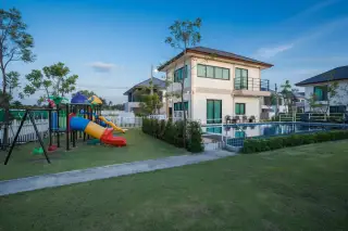 Villa Asiatic two-story house at dusk with illuminated pool, adjacent to a colorful children's playground.