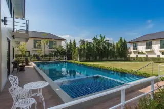 Villa Asiatic view of the rectangular swimming pool with steps, white patio furniture, and surrounding villas.
