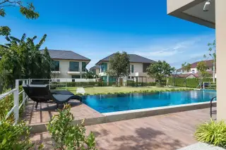 Villa Asiatic outdoor swimming pool with a wooden deck, black lounge chair, and other villas in the background.