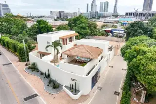 The Sunshine House aerial drone view showing white villa with thatched roof pool area and Pattaya city skyline