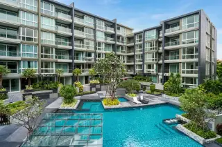 Apus condo building exterior with large lagoon-style pool, glass-bottomed feature and lush tropical courtyard landscaping