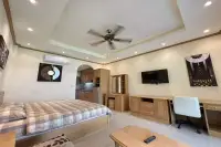 Studio Condo for Sale at Baan Suan Lalana open-plan living area with double bed, wooden furniture, wall-mounted TV, and kitchenette