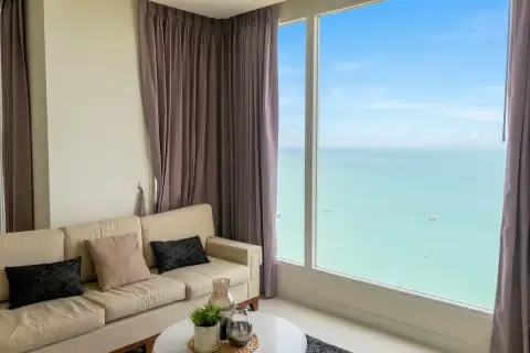 2 Bedroom Condo for Sale at Del Mare bright living room with beige sofa and floor-to-ceiling windows overlooking turquoise ocean