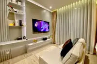 1 Bedroom Condo for Sale & Rent at Arom Wongamat: Living area with sofa, wall-mounted TV, decorative shelves, and light curtains.