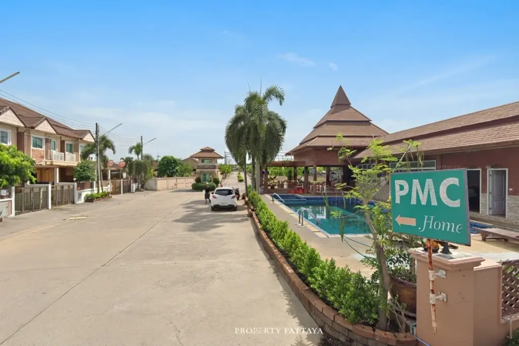 PMC Village 2 street view showing houses, a communal swimming pool, and a clubhouse with a tiered roof.